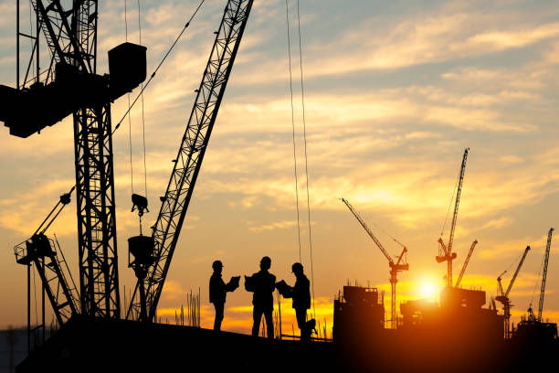 Silhouette of construction workers and cranes at a building site during sunset, representing a professional construction company in Surrey.